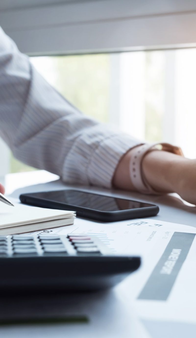 A woman at a desk working through numbers on a calculator, with a notepad and keyboard
