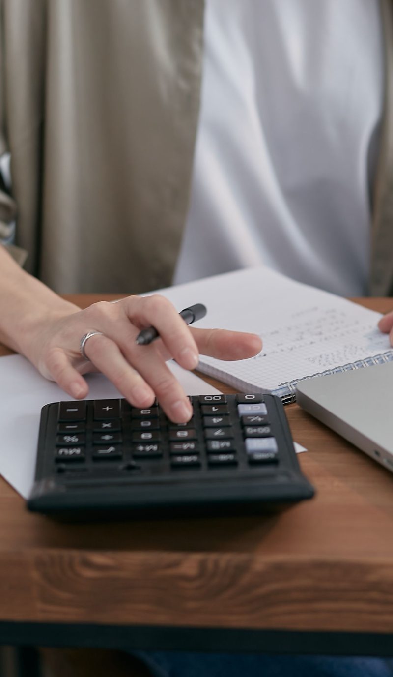 A person at a desk with a calculator, a notepad and a laptop, working through loan balances