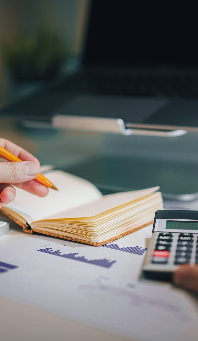 A person working at a desk with a notebook, a calculator and a laptop, reviewing home loan numbers